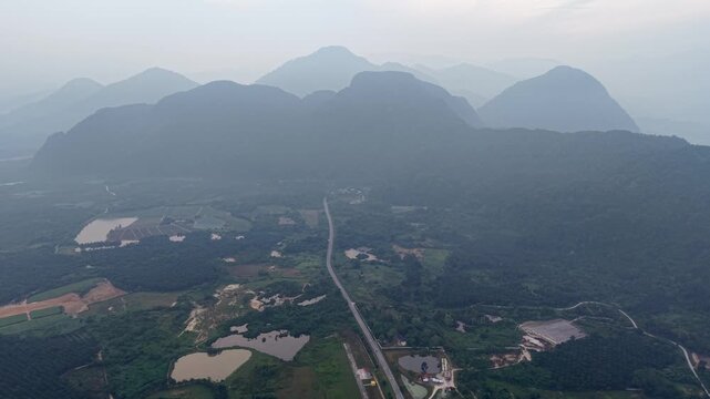 Misty mountains loom over distant hills. Winding road divides lush farmland at Kampar, Perak