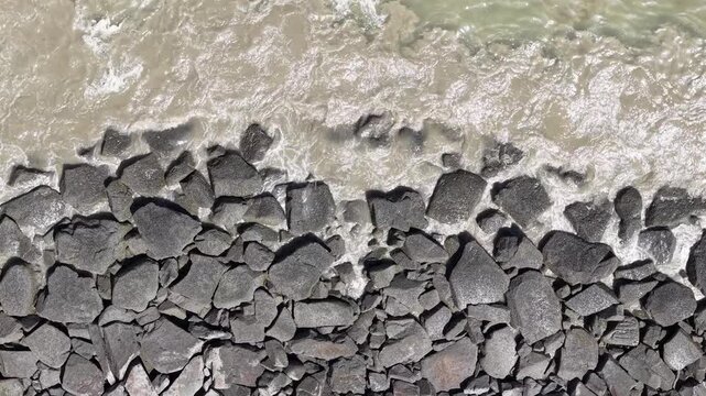 Ocean waves crash onto dark, jagged rocks below. Foam swirls over rough, wet stones