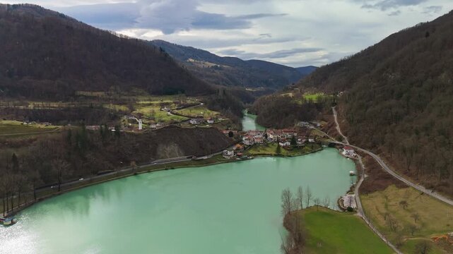 Most na Soči in Slovenia with river, lake, village and church tower in the Soča Valley, surrounded by snowy Julian Alps, forests and mountain roads in a winter drone panorama.