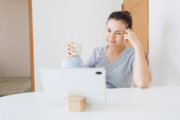Home entertainment with a tablet and coffee. Smiling woman watching the screen during leisure time, using digital technology and online services at home. © soya