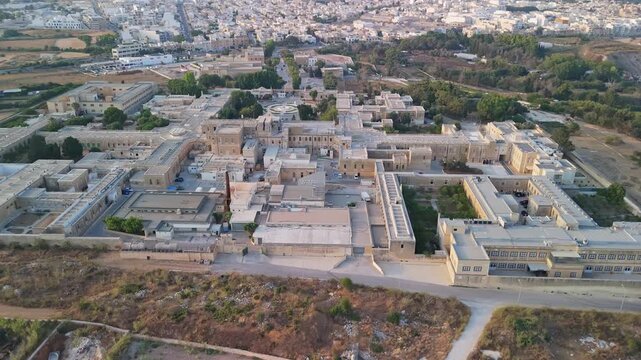 Attard, Malta, Mount Carmel Hospital psychiatric and rehabilitation facility with historic Mediterranean stone buildings, courtyards and gardens in an aerial overview.