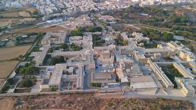 Attard, Malta, Mount Carmel Hospital psychiatric and mental health facility with historic stone architecture, courtyard and gardens in a suburban setting from a panoramic aerial view.