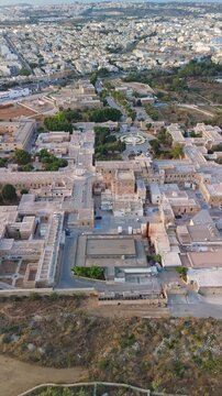 Attard, Malta, Mount Carmel Hospital psychiatric care facility and historic Maltese stone architecture with courtyard and roundabout in urban setting, from a vertical drone perspective.