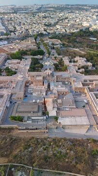 Attard, Malta, Mount Carmel Hospital psychiatric and mental health facility with historic Maltese stone architecture, gardens and surrounding roads in a vertical aerial daytime view.