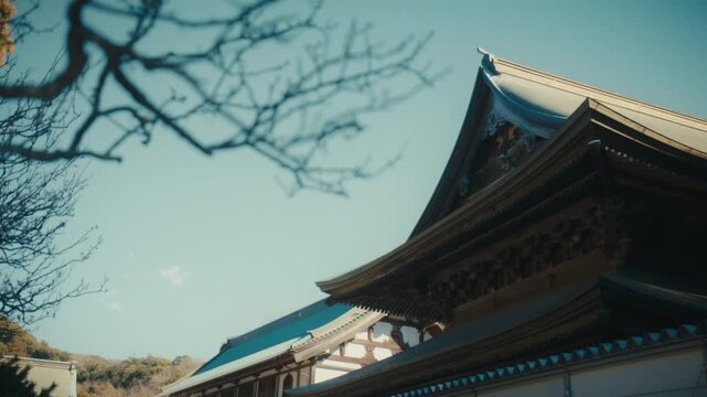 A low-angle view of the historic Sanmon gate's roof architecture at Kencho-ji, Kamakura's oldest Zen temple, showcasing traditional Japanese joinery and weathered copper roofing against a soft winter