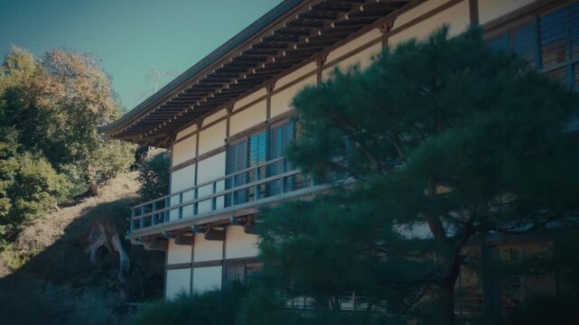 A view of a traditional temple building at Kencho-ji in Kamakura, its wooden veranda and shoji windows framed by pine trees and autumn foliage along a wooded hillside.