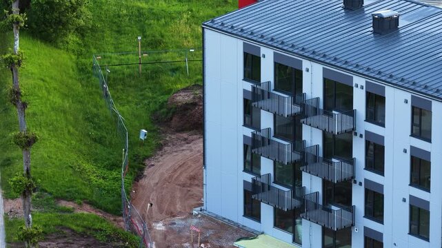 New modern residential building with balconies standing next to an undeveloped construction area