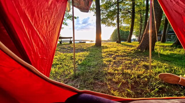 Personal perspective looking out from inside a red camping tent at a forest and lake at sunrise