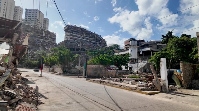 tilt up shot revealing the scale of urban destruction, featuring debris-strewn streets and severely damaged high-rise structures on a coastal hillside.