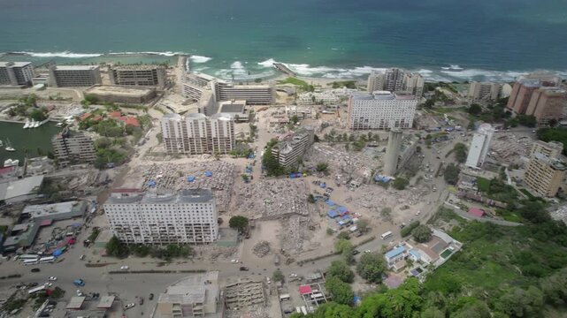 Slow motion drone pan reveals widespread earthquake destruction, collapsed buildings and coastal urban damage in La Guaira, Venezuela.