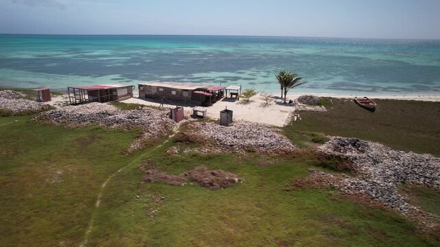 drone tracking shot over a secluded cayo with primitive wooden structures and ancient shell mounds of indigenous heritage amid turquoise waters. La Pelona Dos Mosquises island