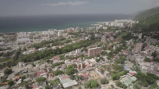 Aerial drone perspective documenting spatial extent of earthquake damage across Caribbean coastal city of La Guaira, Venezuela. Green golf courses in contrast to collapsed buildings