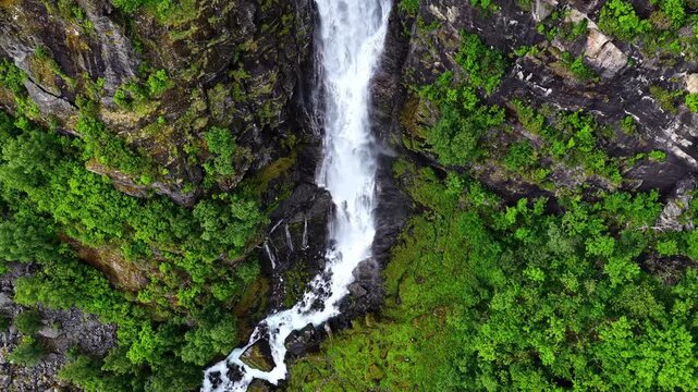 A Spectacular Waterfall Cascades Down Rugged Cliffs Into a Lush Green Valley, Showcasing the Breathtaking Natural Beauty of Fl&aring;m, Aurland, Norway - High Angle Shot
