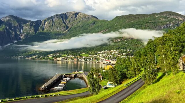 Fl&aring;m, Aurland, Norway - A Breathtaking View of the Tranquil Fjord, Charming Waterfront Village, and Towering Mountains Surrounded by Low-hanging Clouds - Panning Shot