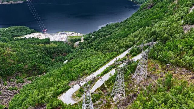 A Scenic Mountain Road Winds Through Lush Green Hills With Towering Power Lines Overlooking a Stunning Norwegian Fjord on the Journey From Oslo to Fl&aring;m, Norway - Wide Shot