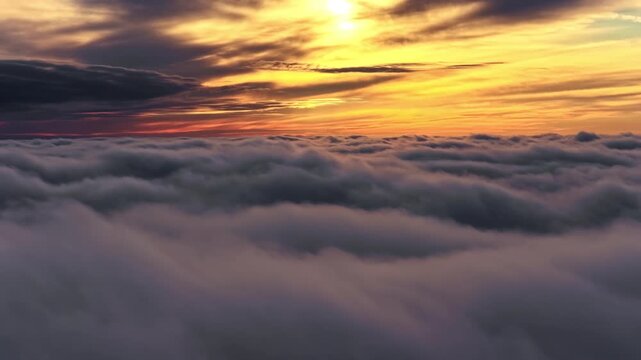 Golden sunlight illuminates thick clouds from above at sunrise or sunset, aerial view