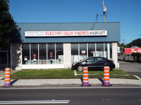 Gatineau, Quebec, Canada &ndash; June 16, 2026: "Electro Deux Freres" storefront with large glass windows, a blue metal upper facade, construction cones, and a parked black car outside at 42 Bd Gr&eacute;ber.
