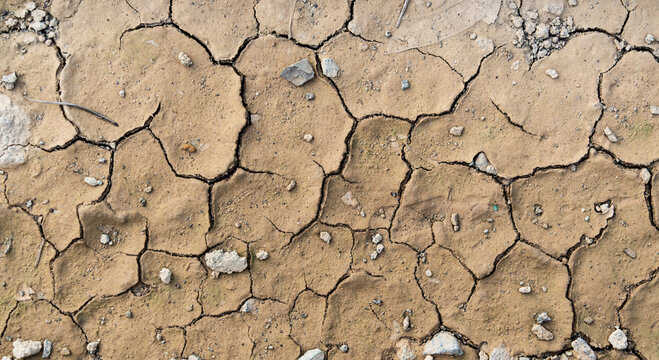 background pattern of cracked dry mud earth surface with small rocks and parched soil texture due to hot weather