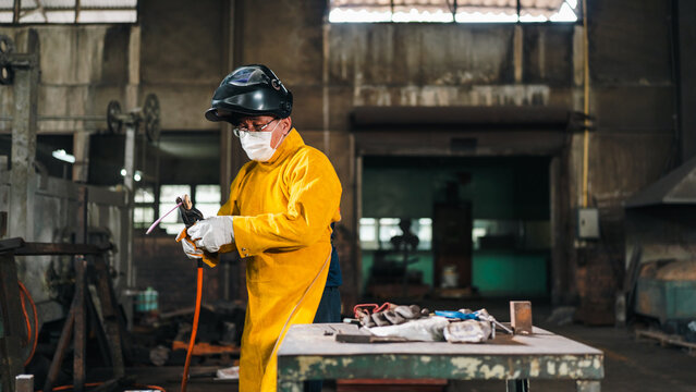 Welder worker helmet mask glove yellow jacket torch workshop metal worker preparing welding torch in industrial interior with focused expression
