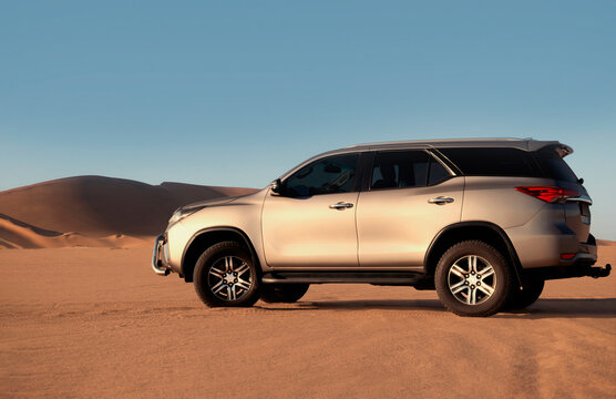 Gray Toyota Fortuner standing among the golden sands of the Namib Desert under a bright sky, capturing the spirit of off-road adventure, freedom, travel, and exploration in Namibia. 