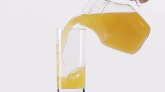 Fresh orange juice slowly pouring from a glass pitcher into a tall drinking glass, isolated on a clean white background. Healthy lifestyle and vitamin C concept for a nutritious breakfast