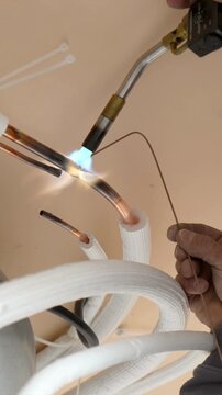 Technician welding copper pipes for air conditioner installation.