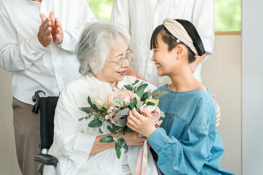 A smiling granddaughter presents a bouquet of flowers to her grandmother in a wheelchair.