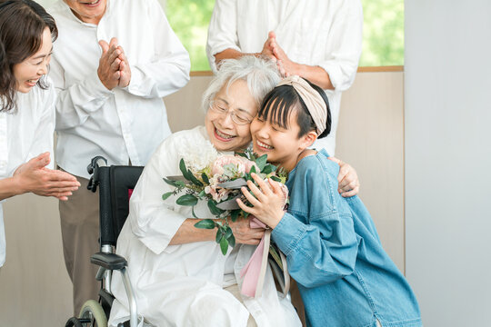 A smiling granddaughter presents a bouquet of flowers to her grandmother in a wheelchair.