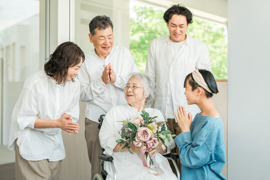 A three-generation family visits their grandmother in a care facility and presents her with a bouquet of flowers as a get-well gift.