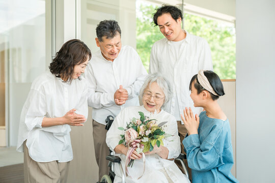 A three-generation family visits their grandmother in a care facility and presents her with a bouquet of flowers as a get-well gift.
