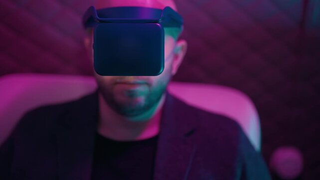 Serious bald man with a beard wearing a futuristic virtual reality headset, experiencing an immersive digital world with magenta and cyan neon lights reflecting on his face and the device