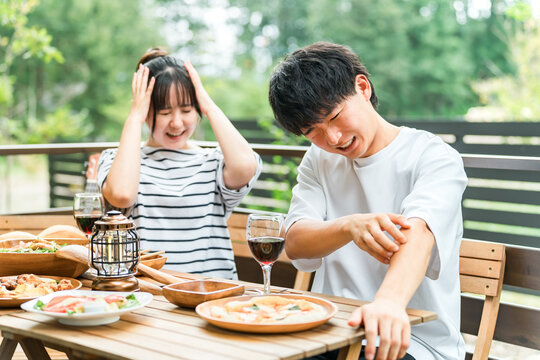 A couple is having trouble with insect bites while eating outdoors.