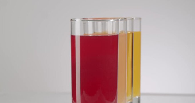 Row of glasses filled with various colorful fruit juices, such as orange, apple, grapefruit, and cherry, gradually emptying on a clean white background, symbolizing a refreshing break.