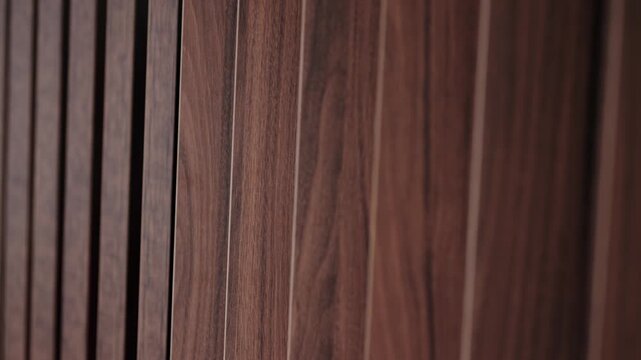 Rhythmic pattern of vertical dark brown wood panels creating a textured background, with a subtle camera movement revealing depth and shadow for a sophisticated interior design concept
