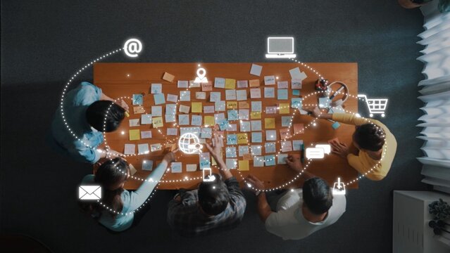 A diverse team collaborates over a table filled with sticky notes, integrating technology and communication tools for effective project planning in a modern office. Raster
