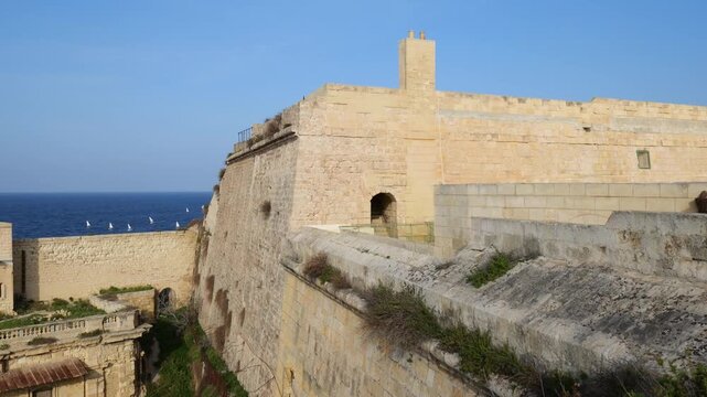 fort st elmo bastion wall watchtower limestone rampart sailing dinghies horizon mediterranean sea clear blue sky valletta malta coastal fortification star fort defensive architecture panorama