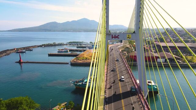 A breathtaking aerial perspective of Soekarno Bridge in Manado. Vehicles traverse this essential cable-stayed bridge, highlighting the city's vibrant harbor and beautiful mountainous horizon.