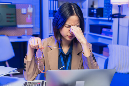 Young Asian businesswoman suffering from eye strain while working on laptop in office.