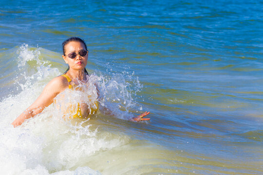 Woman in yellow swimsuit happy with wave on beach