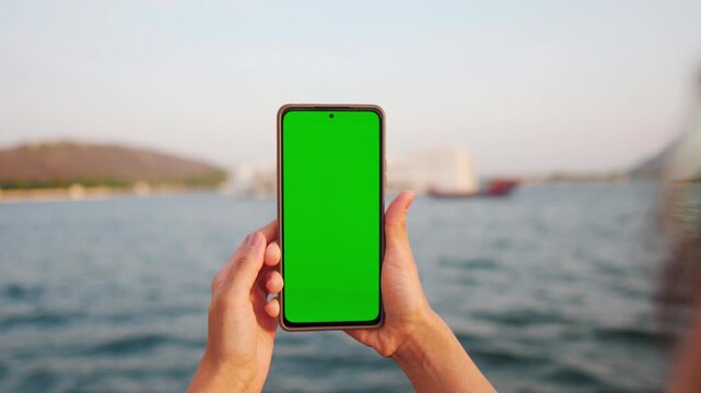 4K Shot of tourist female holding smartphone with blank green screen against Lake Pichola at Udaipur, India. Chroma key, close up Indian woman hand holding phone with vertical green screen. Outdoor tr