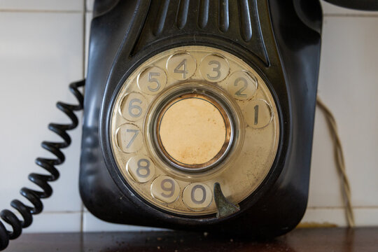 Antique black rotary dial telephone close-up showing numbers and coiled cord against a tiled wall
