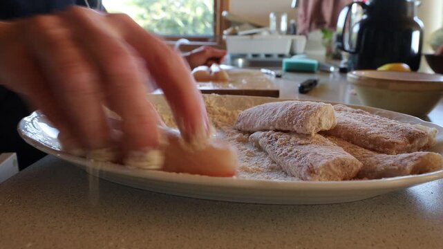 Hirtshals, Denmark A cook rolls white fish fillets in flour in a plate for frying in a pan. 