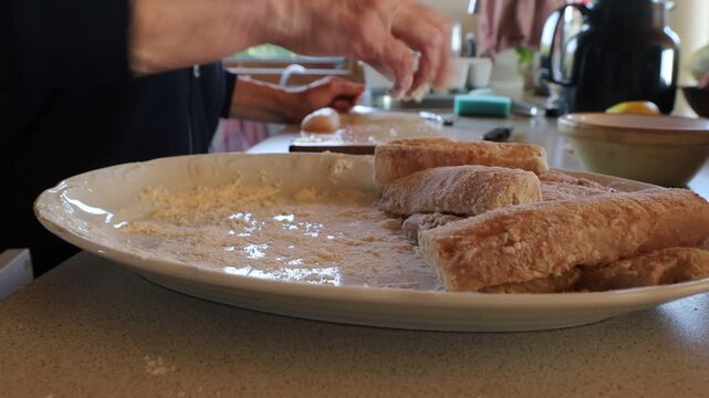 Hirtshals, Denmark A cook rolls white fish fillets in flour in a plate for frying in a pan. 