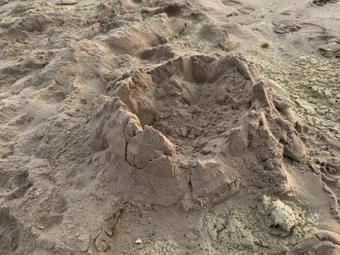 Collapsed sandcastle on sandy beach showing erosion and weathered remains