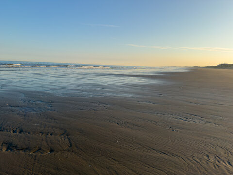 Expansive sandy beach at low tide with gentle waves and clear evening sky