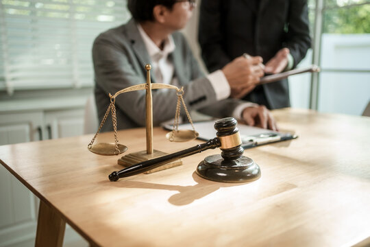 Gavel and scales of justice on a desk with blurred lawyers discussing in a law office, showing legal advice, court, and business meeting concepts