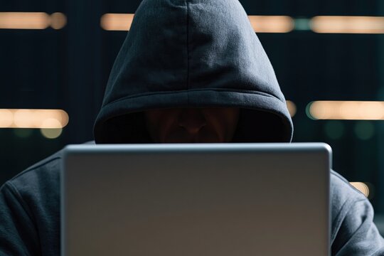 Hacker in a hoodie using a laptop in darkness to commit a cyber crime for privacy