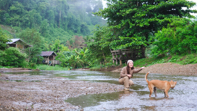 A woman playing with a dog by the river in rural village