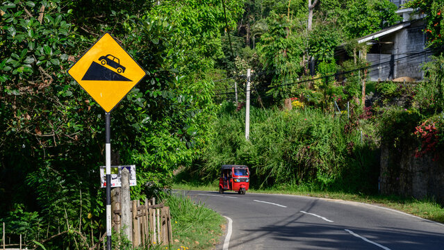 Steep downhill road warning sign with tuk-tuk on a scenic road in Nuwara Eliya, Sri Lanka
