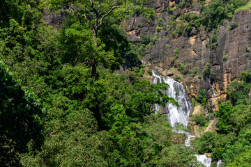 Waterfall cascades down rugged rocky cliffs surrounded by lush green forest in the highlands of Nuwara Eliya, Sri Lanka © nilanka